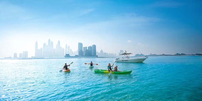 People kayaking and boating in the clear blue waters off the Dubai coast with city skyline in the background during the summer season