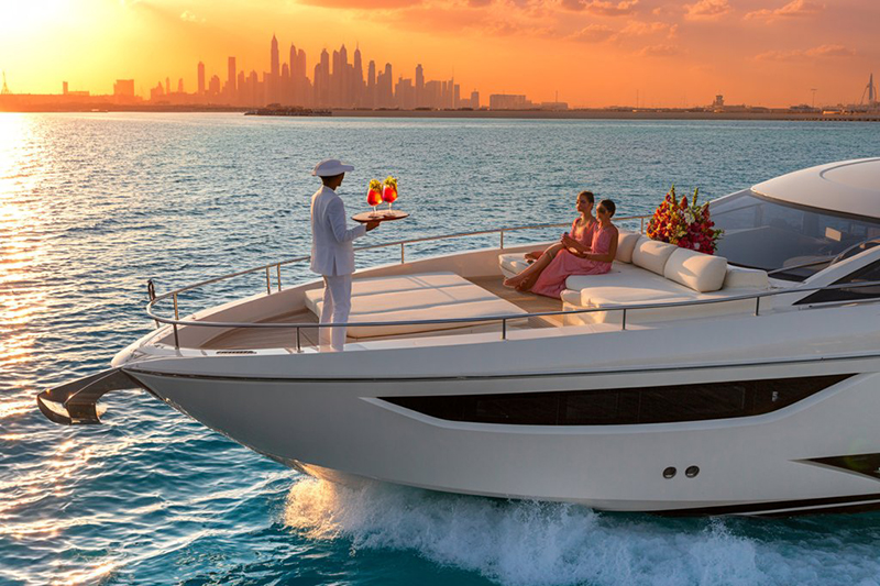 A steward serving drinks to guests on the bow of a luxury yacht with the Dubai skyline at sunset, highlighting the exquisite service available with Dubai yacht rental.